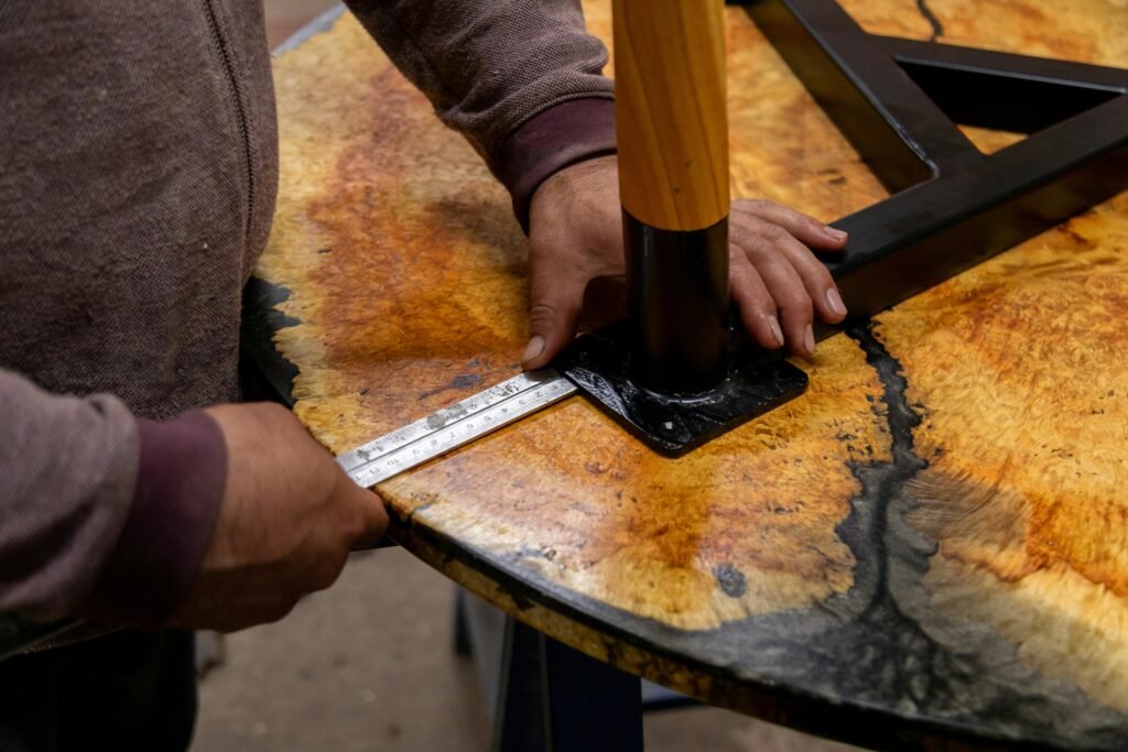 Craftsman measuring wooden table with ruler in workshop.
